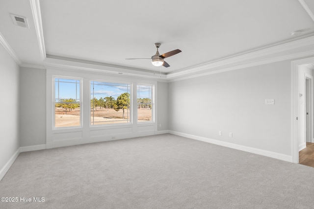 carpeted spare room featuring ceiling fan, visible vents, baseboards, ornamental molding, and a tray ceiling