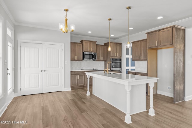 kitchen featuring light countertops, hanging light fixtures, appliances with stainless steel finishes, a kitchen island with sink, and a kitchen bar