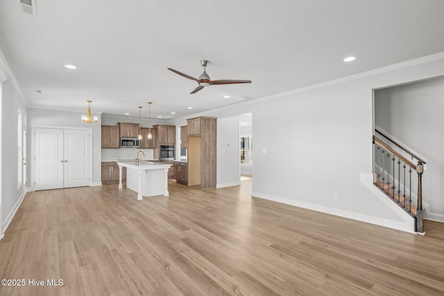 unfurnished living room featuring light wood finished floors, visible vents, ceiling fan, stairs, and crown molding