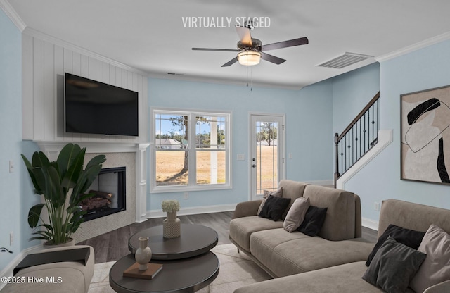 living area with a premium fireplace, wood finished floors, visible vents, ornamental molding, and stairway