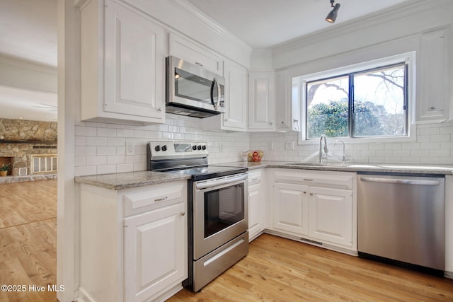 kitchen featuring appliances with stainless steel finishes, tasteful backsplash, sink, white cabinets, and light hardwood / wood-style floors