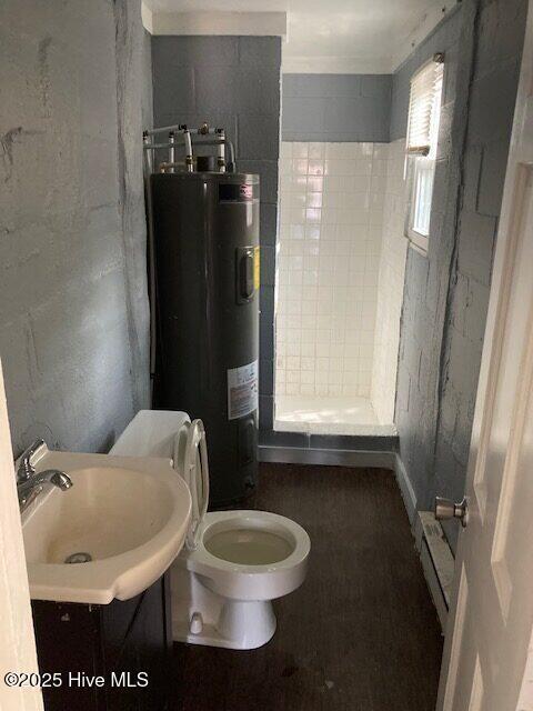 bathroom with tiled shower, vanity, toilet, and electric water heater