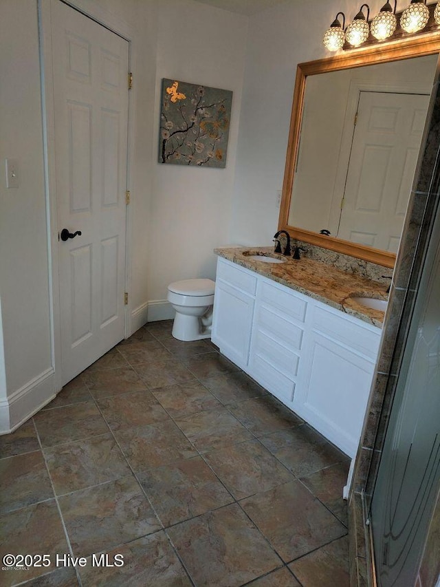 full bathroom featuring double vanity, baseboards, toilet, and a sink