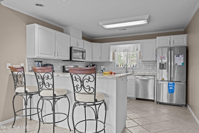 806 Lord Granville Dr, Morehead City, NC 28557 - kitchen featuring stainless steel appliances, a peninsula, decorative backsplash, ornamental molding, and white cabinets