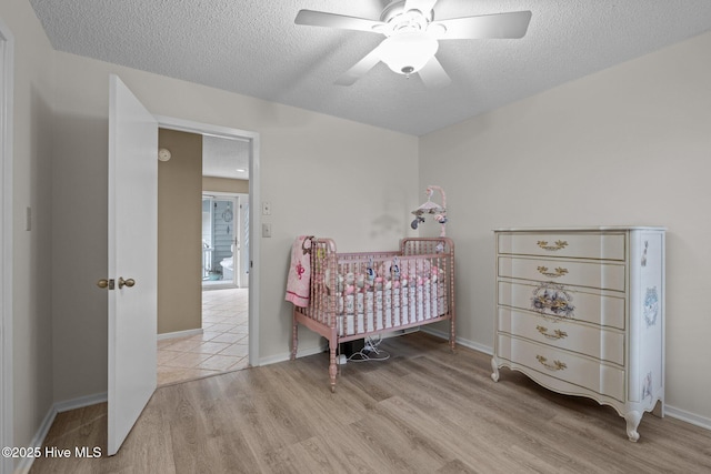 806 Lord Granville Dr, Morehead City, NC 28557 - bedroom featuring light wood-style flooring, a textured ceiling, a crib, a ceiling fan, and baseboards