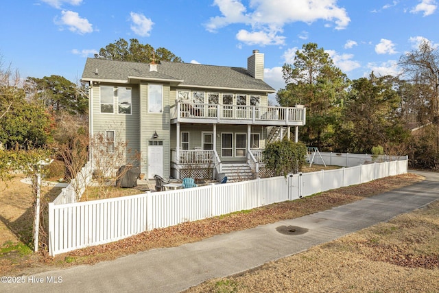 806 Lord Granville Dr, Morehead City, NC 28557 - rear view of property featuring a chimney, a fenced front yard, a wooden deck, a shingled roof, and a porch