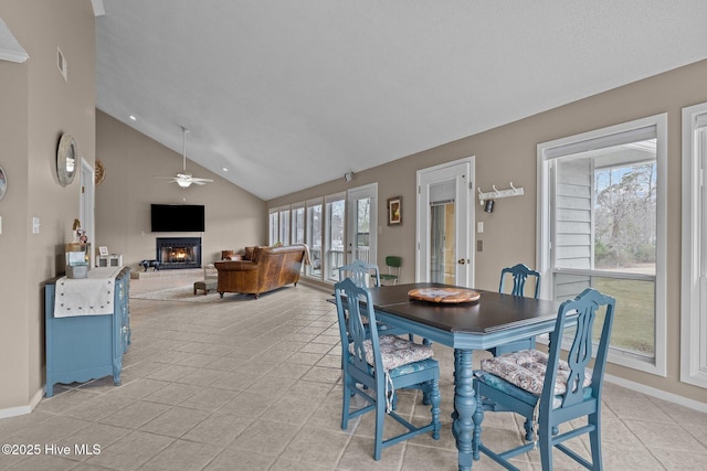 806 Lord Granville Dr, Morehead City, NC 28557 - dining space featuring a warm lit fireplace, a ceiling fan, healthy amount of natural light, light tile patterned flooring, and high vaulted ceiling