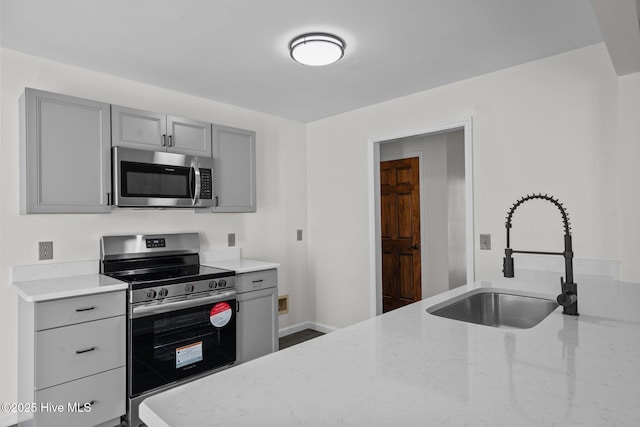 kitchen with light stone countertops, gray cabinets, stainless steel appliances, and a sink