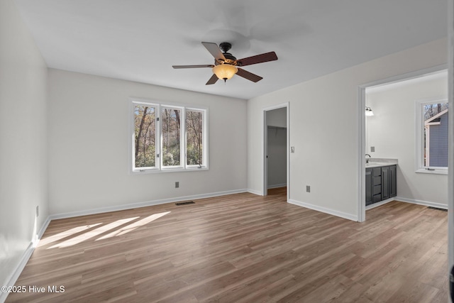 unfurnished bedroom featuring baseboards, visible vents, connected bathroom, wood finished floors, and a walk in closet