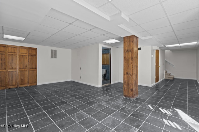 finished below grade area with stairs, a paneled ceiling, visible vents, and baseboards