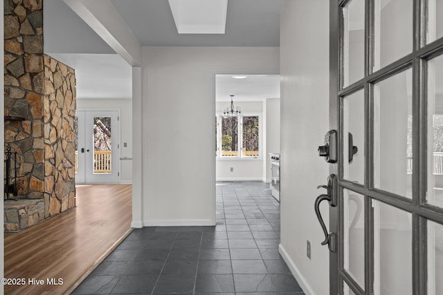 corridor with dark tile patterned floors, an inviting chandelier, and baseboards