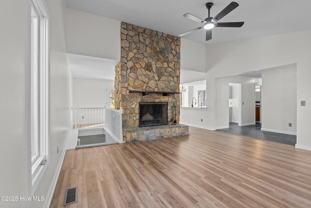 unfurnished living room with visible vents, a ceiling fan, a stone fireplace, wood finished floors, and baseboards