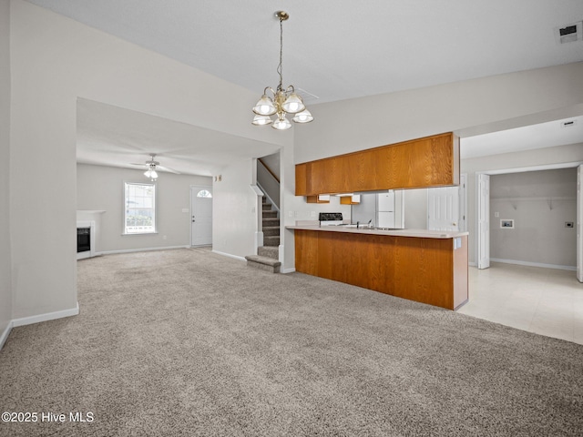 kitchen with lofted ceiling, ceiling fan with notable chandelier, decorative light fixtures, light colored carpet, and kitchen peninsula