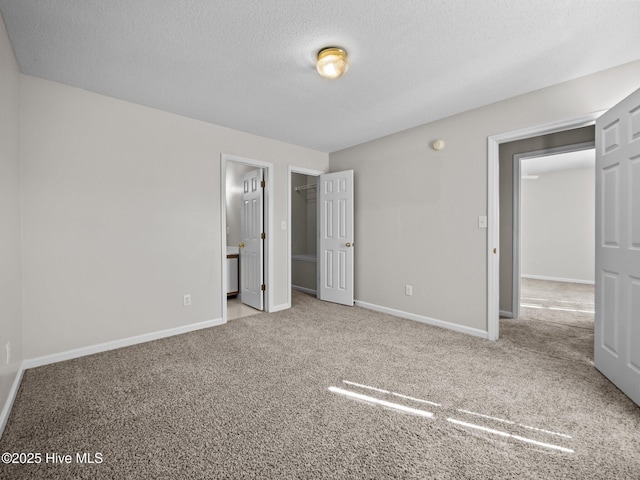 unfurnished bedroom featuring light carpet, ensuite bath, a walk in closet, and a textured ceiling