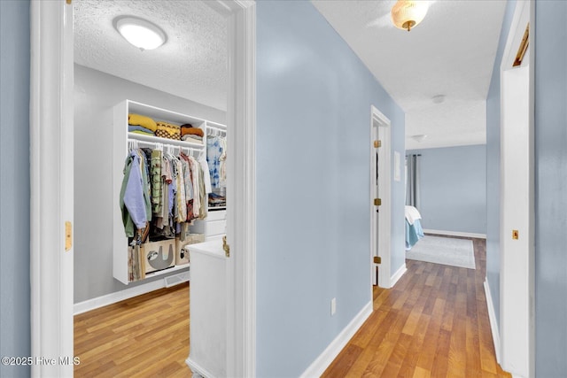 hallway with light wood-type flooring, baseboards, and a textured ceiling