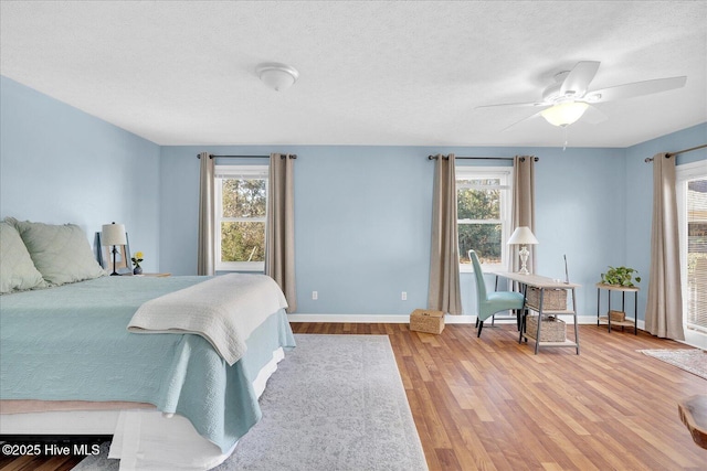 bedroom with a textured ceiling, multiple windows, wood finished floors, and baseboards