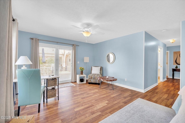 living area featuring ceiling fan, a textured ceiling, baseboards, and wood finished floors