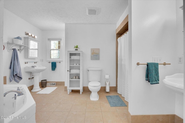 full bathroom with visible vents, toilet, tile patterned floors, a garden tub, and a textured ceiling