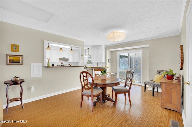 dining area featuring baseboards, visible vents, light wood-style flooring, and a textured ceiling