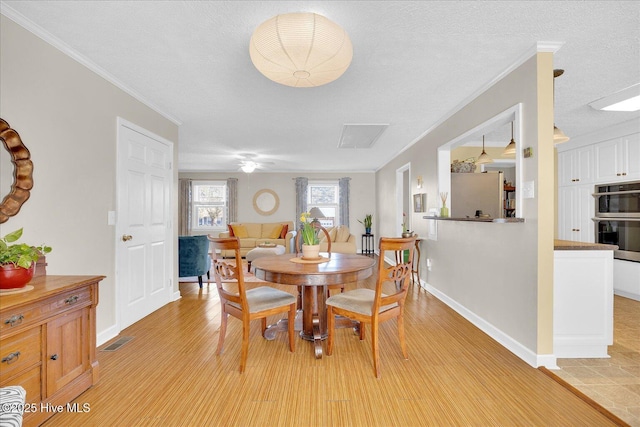 dining room featuring light wood-style floors, baseboards, ornamental molding, and a textured ceiling