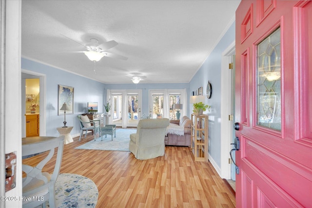 foyer entrance featuring ornamental molding, ceiling fan, light wood-style flooring, and a textured ceiling