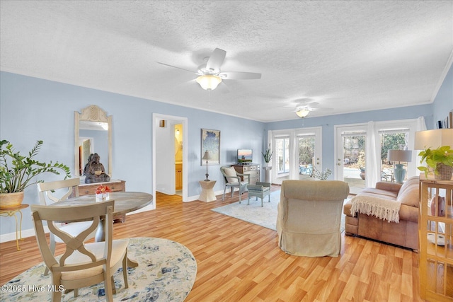 living room with a textured ceiling, ceiling fan, light wood-type flooring, and baseboards