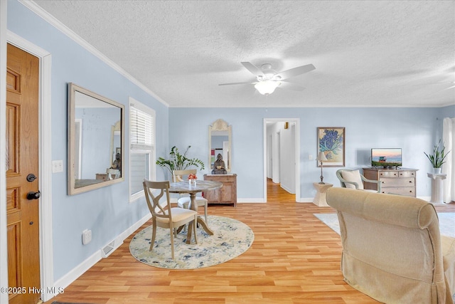 dining area with light wood-style flooring, ornamental molding, ceiling fan, a textured ceiling, and baseboards