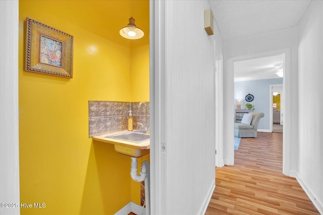 hallway featuring light wood-style floors, a sink, and baseboards