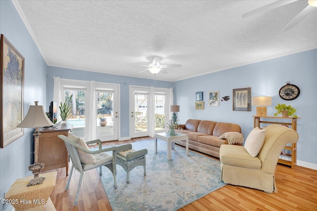 living area featuring a ceiling fan, baseboards, ornamental molding, and light wood finished floors