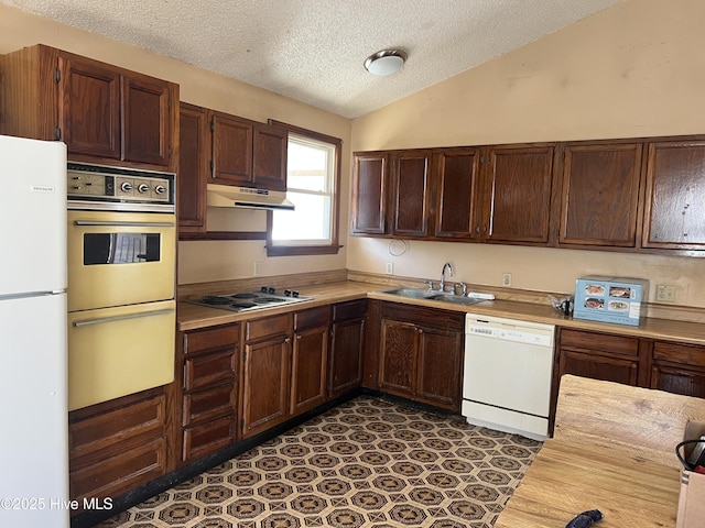 kitchen featuring white appliances, vaulted ceiling, light countertops, under cabinet range hood, and a sink