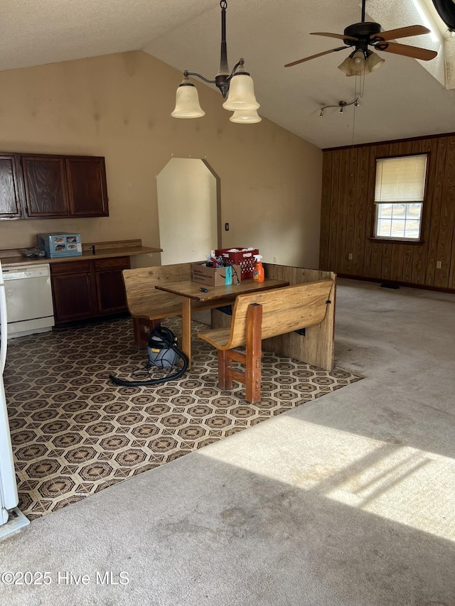 dining space featuring carpet floors, ceiling fan, wooden walls, and vaulted ceiling