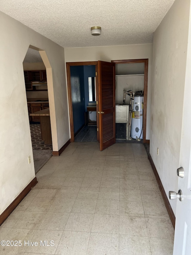 empty room featuring water heater, a textured ceiling, arched walkways, and baseboards