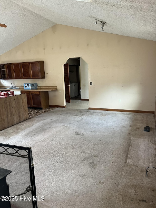 interior space with arched walkways, light carpet, vaulted ceiling, a textured ceiling, and baseboards