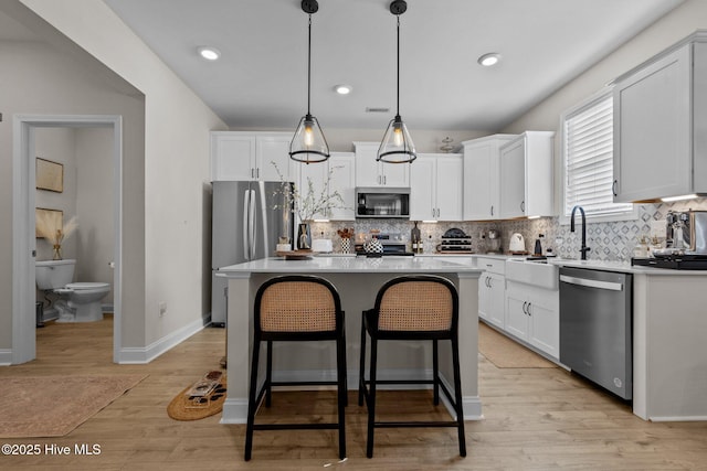 kitchen with white cabinetry, stainless steel appliances, a kitchen island, and decorative light fixtures