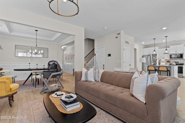 living room with crown molding, a notable chandelier, light hardwood / wood-style floors, and a raised ceiling