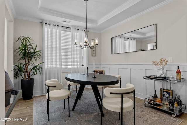 dining space with light hardwood / wood-style flooring, a raised ceiling, and an inviting chandelier