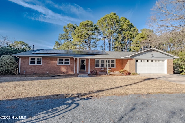 single story home featuring a garage, roof mounted solar panels, brick siding, and driveway