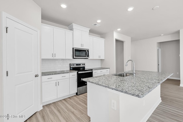 kitchen with appliances with stainless steel finishes, sink, white cabinets, a kitchen island with sink, and light stone counters