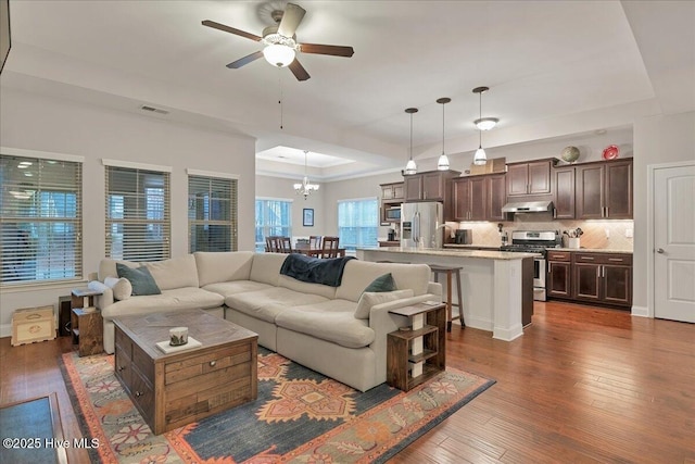 living area with a raised ceiling, visible vents, dark wood finished floors, and ceiling fan with notable chandelier