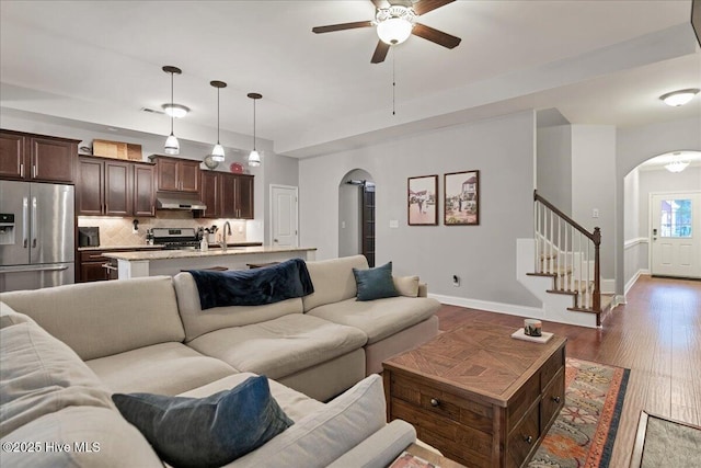 living area with arched walkways, baseboards, a ceiling fan, stairway, and wood finished floors