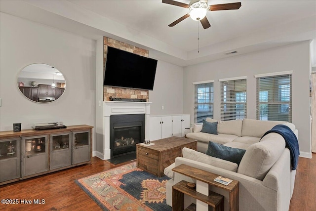 living area featuring visible vents, baseboards, a ceiling fan, a fireplace with flush hearth, and wood finished floors