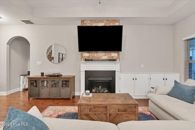 living area featuring a fireplace with raised hearth, visible vents, arched walkways, and wood finished floors