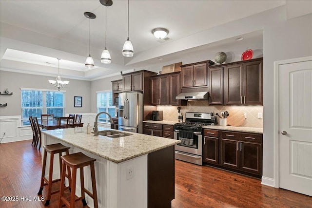 kitchen featuring a raised ceiling, appliances with stainless steel finishes, a sink, dark brown cabinets, and under cabinet range hood