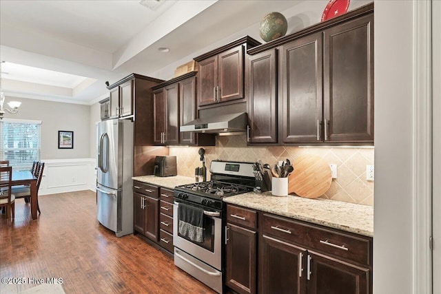 kitchen with a raised ceiling, decorative backsplash, appliances with stainless steel finishes, dark brown cabinets, and ventilation hood