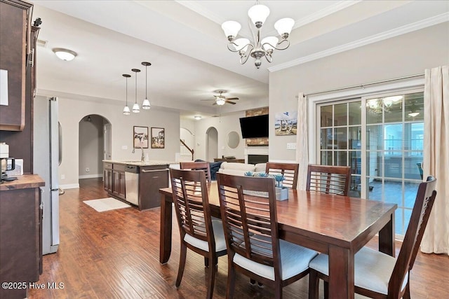 dining space with ceiling fan with notable chandelier, arched walkways, dark wood-type flooring, and ornamental molding