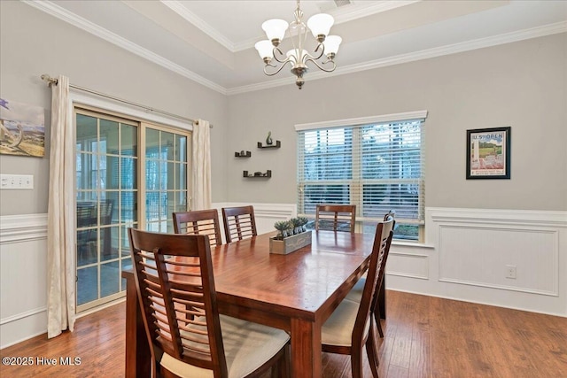 dining area with wood finished floors, ornamental molding, wainscoting, a raised ceiling, and an inviting chandelier