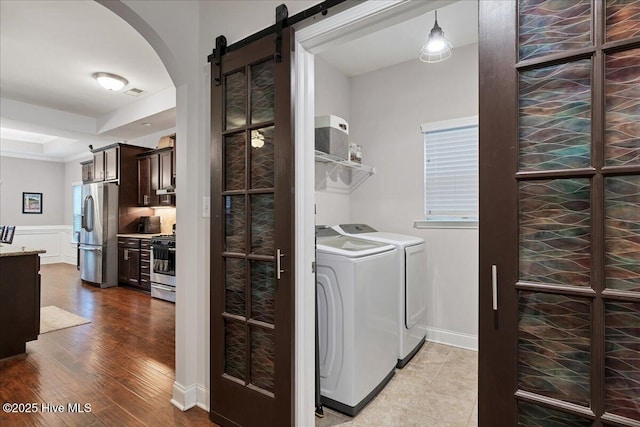 clothes washing area with laundry area, a barn door, arched walkways, wood finished floors, and separate washer and dryer