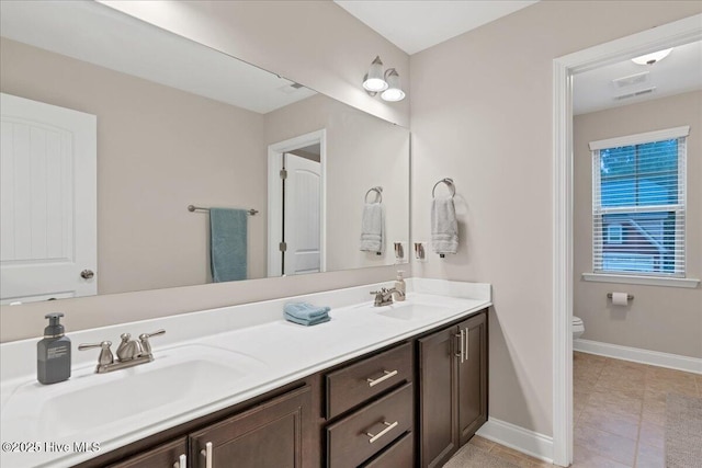 full bathroom featuring toilet, a sink, baseboards, and double vanity