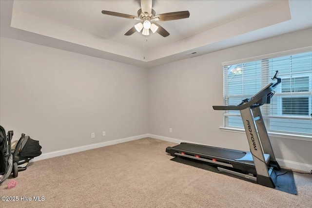 exercise area featuring carpet floors, a tray ceiling, and baseboards