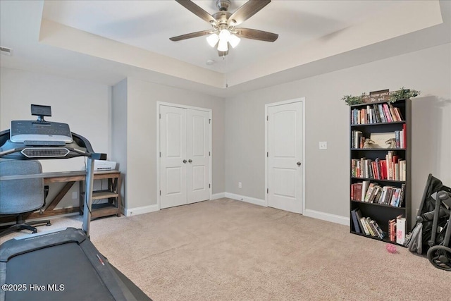 workout area with ceiling fan, visible vents, baseboards, a tray ceiling, and carpet